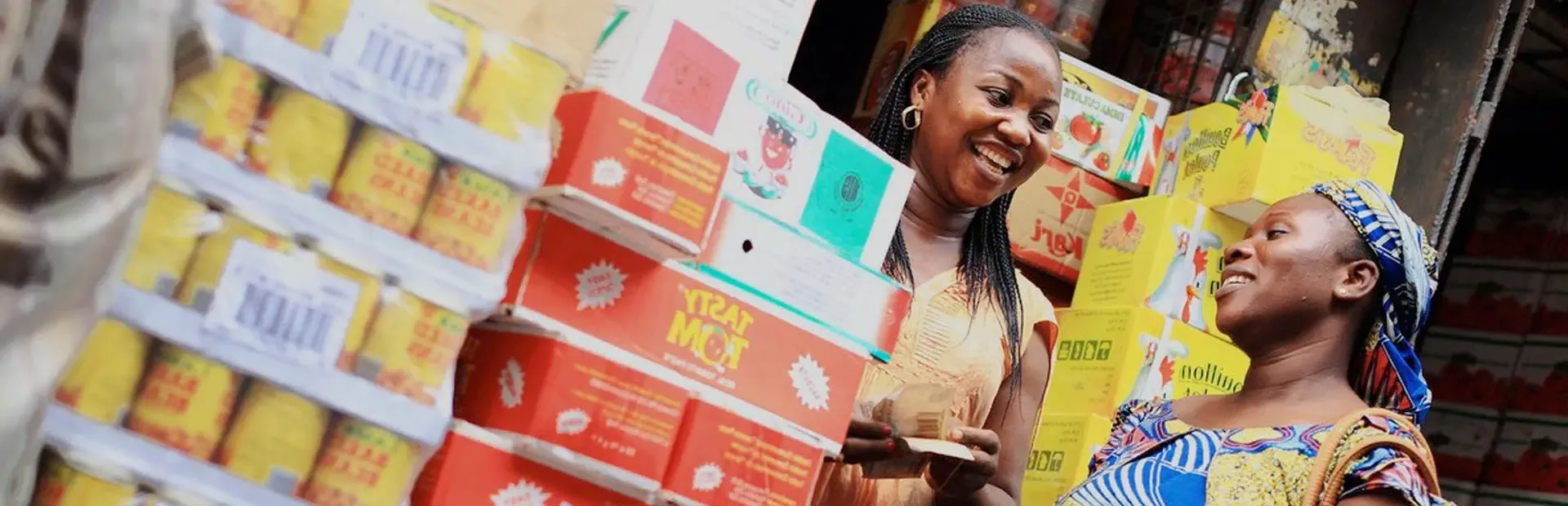 Customer buying packaged foods from a shop owner at her stall, Nigeria, Olam. 